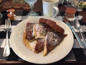 french toast and sausage on white plate with silverware on table